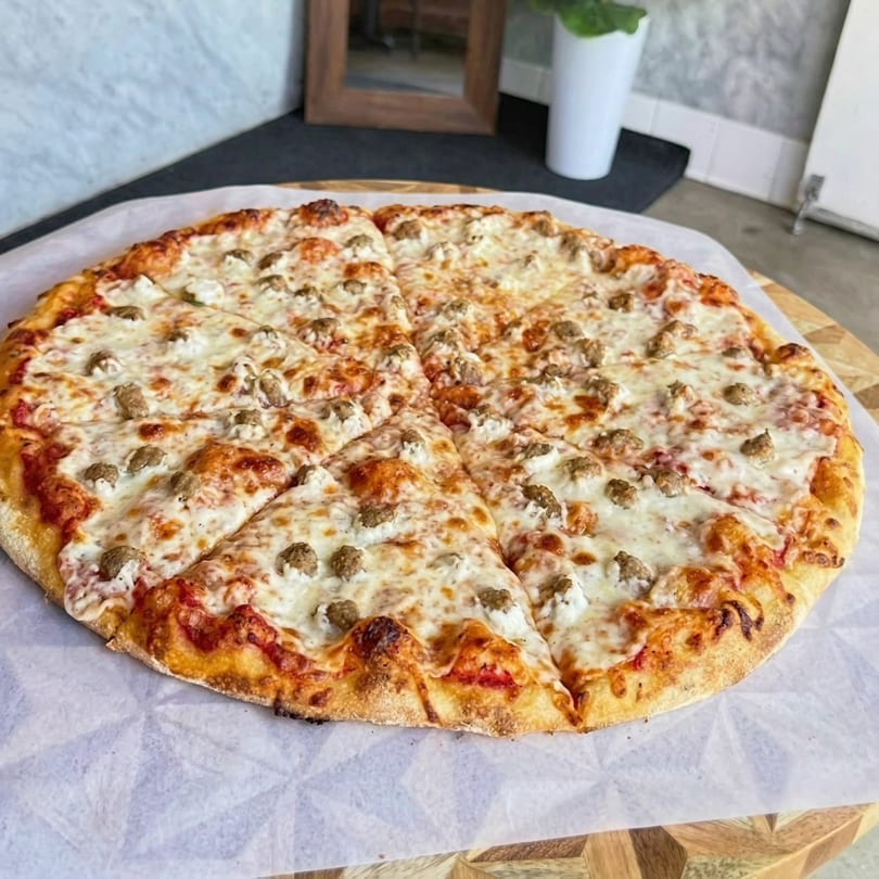 A whole, sliced pizza with melted cheese, tomato sauce, and sausage crumbles on parchment paper.