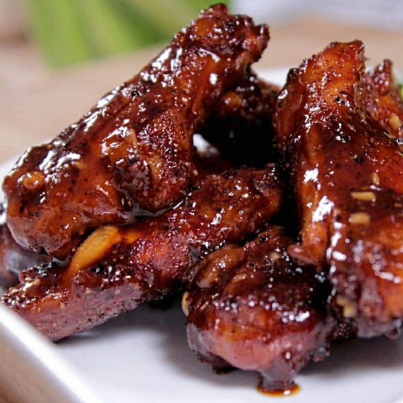 Close-up of several glossy, dark brown chicken wings coated in a rich sauce on a white plate.